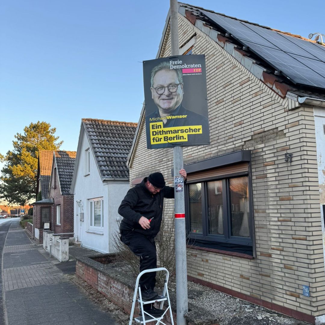 Mann steht auf Leiter und hängt Plakat auf